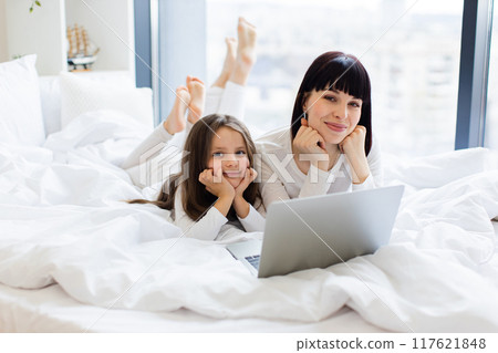 Mother and daughter relaxing on bed with laptop 117621848