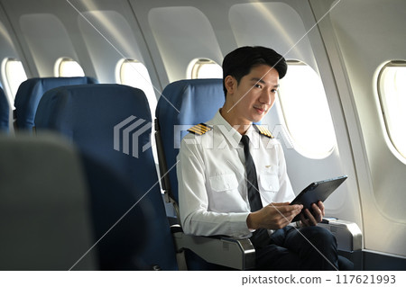 Handsome asian pilot sitting in an airplane seat and reviewing flight plans on digital tablet 117621993