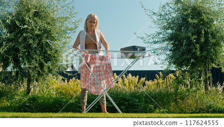 Middle-aged woman hanging clothes to dry on a sunny day in her backyard. 117624555