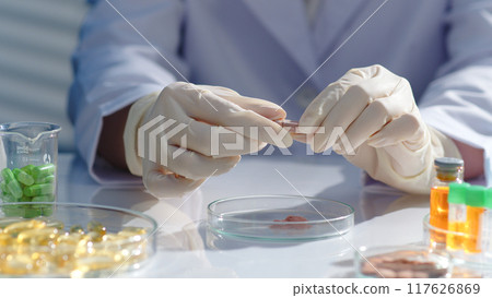 The researcher hands are holding a capsule and preparing to break it. Drug research scene, surrounded by lab glassware containing many different types of drugs. Scene for advertising The researcher hands are holding a capsule and preparing to break it. Drug research scene, surrounded by lab glassware containing many different types of drugs. Scene for advertising 117626869