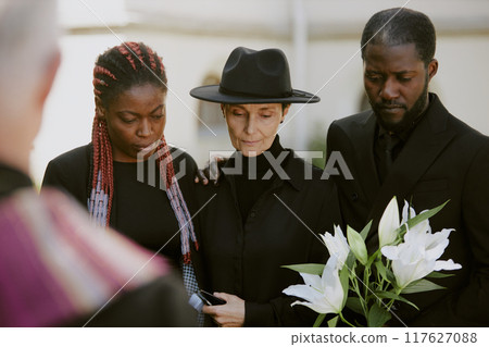 Biracial family dressed in mourning clothes looking at grave at bemoaning about their loss 117627088