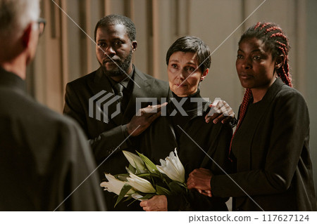 Biracial family listening to pastors words in church before burial ceremony 117627124