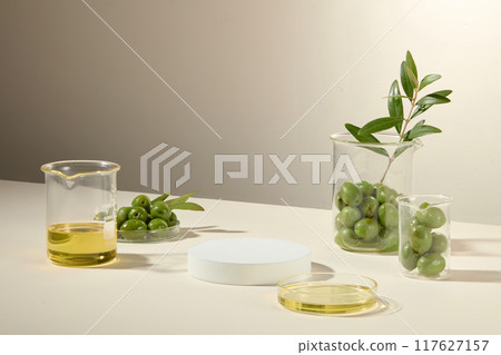 Olives, branches, and essential oils are filled into beakers and petri dishes, with a white platform displaying cosmetic products as a natural ingredient. Minimal advertisement Olives, branches, and essential oils are filled into beakers and petri dishes, with a white platform displaying cosmetic products as a natural ingredient. Minimal advertisement 117627157