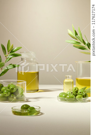 Olive fruit, olea Europaea oil are filled in transparent petri dishes, glass jars and beaker. Garnished with olive leaves to create a minimalist layout for advertising. 117627174