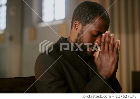 African American Man sitting on wooden bench and praying to God during burial service African American Man sitting on wooden bench and praying to God during burial service 117627175