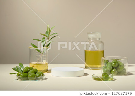 A glass bowl and petri dish filled with fresh green olives, and a larger glass jar and beaker with an olive branch filled with oil. Natural concept for beauty care product 117627179