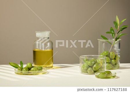 Olives and extract are placed in various containers such as beakers, petri dishes, and glass jars, with a designated space in the middle for the product. Cosmetics advertisement. Olives and extract are placed in various containers such as beakers, petri dishes, and glass jars, with a designated space in the middle for the product. Cosmetics advertisement. 117627188