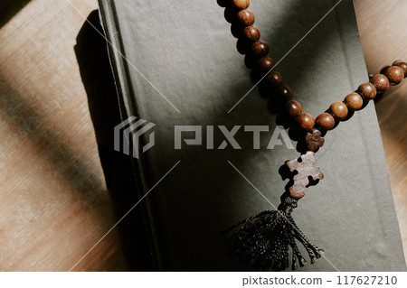 Top down shot of bible with black cover and wooden rosary with cross on wooden table 117627210