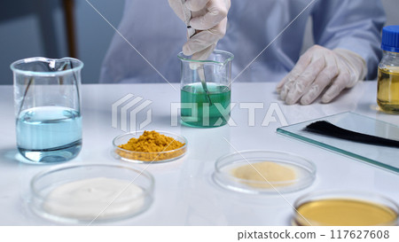 The researcher is using tweezers to pick up a sample of damaged hair and dip it into a green solution for testing. Scientific scene, laboratory research for hair products, repair damaged hair The researcher is using tweezers to pick up a sample of damaged hair and dip it into a green solution for testing. Scientific scene, laboratory research for hair products, repair damaged hair 117627608