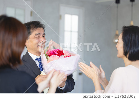 A father receiving a bouquet of flowers from his family on his retirement 117628302