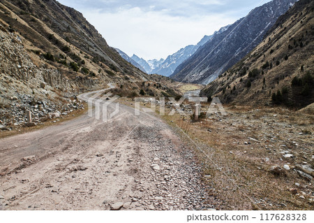 Rocky gravel road in the hillside leading into the mountains. 117628328