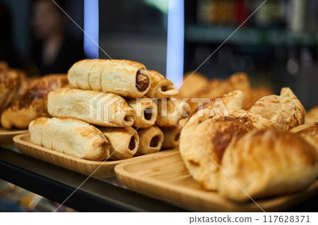 Golden puff pastry baked in oven. Samsa, sausages in dough Varied selection of pastries and snacks in coffee shop. Golden puff pastry baked in oven. Samsa, sausages in dough Varied selection of pastries and snacks in coffee shop. 117628371