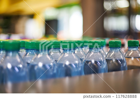 Blue plastic half-liter small volume water bottles with green cap lid in store, supermarket shelf, close up. 117628888
