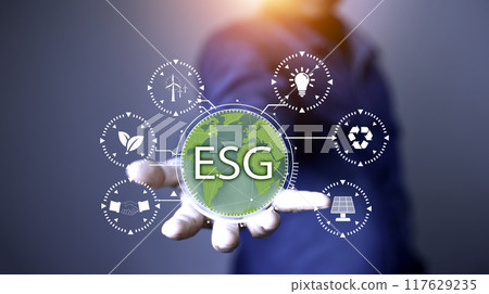Net zero 2050 ESG concept, Hand with green world, wind energy system icon on blurred green leaf background. wind energy for green environment. Businessman background with energy icons around. 117629235