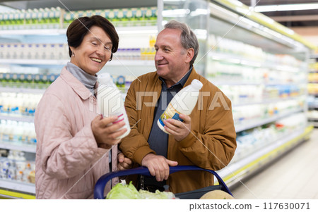 Mature couple choosing jug of milk in dairy department in grocery store 117630071