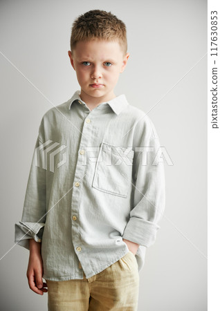 Portrait of young sad boy keeping hand in pocket, looking to the camera. Serious kid in casual clothes posing on white background. Portrait of young sad boy keeping hand in pocket, looking to the camera. Serious kid in casual clothes posing on white background. 117630853
