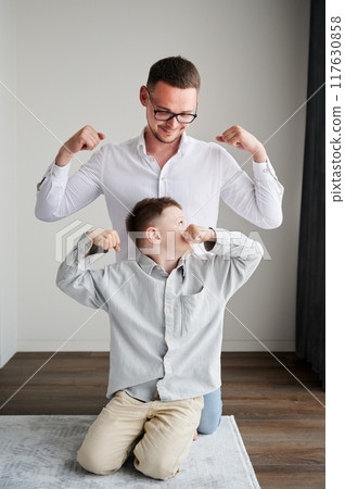 Young father playing with his curious son. Funny kid showing muscles to his dad. Family enjoying activity games at home. 117630858