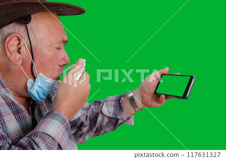 Health Concerns of the Elderly: Farmer in Brown Hat Using Telemedicine, Coughing into Napkin to Prevent Germ Spread, Tanned Face, Green Screen for Easy Editing. Health Concerns of the Elderly: Farmer in Brown Hat Using Telemedicine, Coughing into Napkin to Prevent Germ Spread, Tanned Face, Green Screen for Easy Editing. 117631327