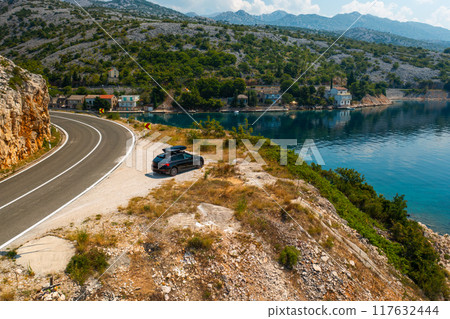 Aerial view of car with a roof box stands on the side of a cliff and beautiful rocks in the background Aerial view of car with a roof box stands on the side of a cliff and beautiful rocks in the background 117632444