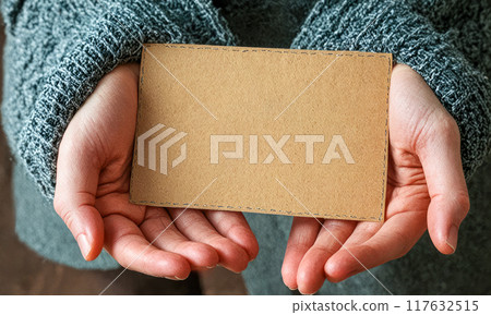 Invitation Card Held in Hands, mockup Brown Paper Invite, Grey Sweater Background. Autumn winter, cold weather 117632515