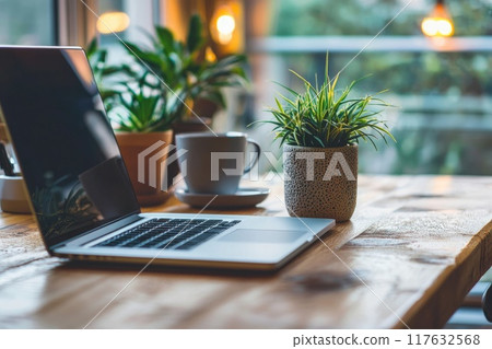 A laptop is open on a wooden table with a potted plant and a cup of coffee, Concept of productivity and relaxation 117632568