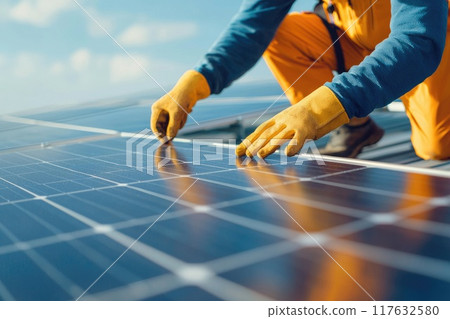 A man in orange pants and a yellow glove is working on a solar panel, green energy and sustainable power technology 117632580