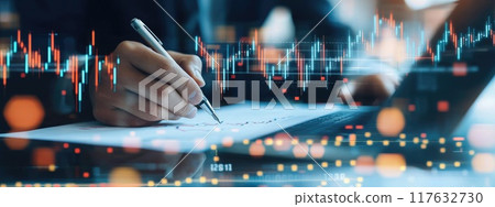 A hands holding a pen and writing on white paper surrounded by stock market charts and graphs showing growth in business success 117632730
