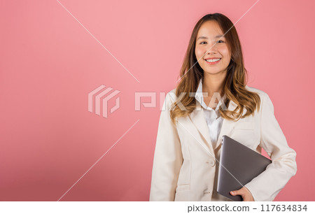 Business woman smiling confident smiling holding closed laptop, Portrait excited happy Asian young female person hugging close cover computer device studio shot isolated on pink background Business woman smiling confident smiling holding closed laptop, Portrait excited happy Asian young female person hugging close cover computer device studio shot isolated on pink background 117634834