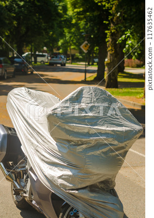 A motorcycle covered with an awning stands near a forged fence in the park. High quality photo 117635462