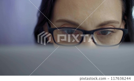 Woman with glasses engaged in reading or work, conveying concentration. Front view and close up portrait Woman with glasses engaged in reading or work, conveying concentration. Front view and close up portrait 117636244