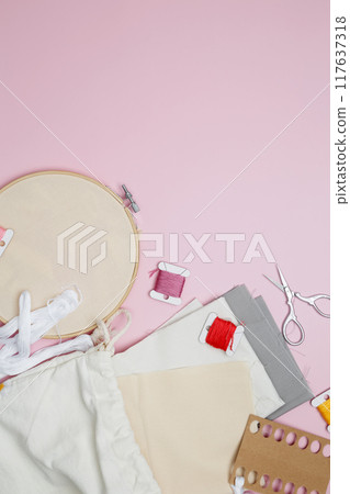 Embroidery set fot stitching. Beige cotton cloth in embroidery hoop on pink background with fabric, colorful threads, scissors and needls 117637318