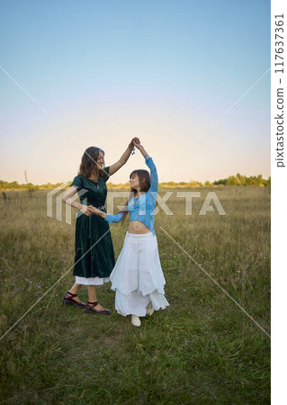 two woman in  whimsical aesthetic style dress  dance in a field in the summer at a sunset 117637361