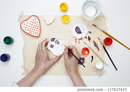 A woman paints clay products. Hobby clay modeling A woman paints clay products. Hobby clay modeling 117637425