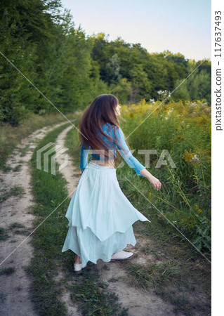 woman in whimsical aesthetic style dress in field in summer at sunset 117637493