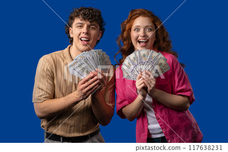 Rich couple, USD currency. Young man and woman with money on blue, happy pair Rich couple, USD currency. Young man and woman with money on blue, happy pair 117638231