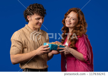 Young woman gives gift box to husband or boyfriend. Surprise, unexpected present. Birthday, celebration, surprise, anniversary concept. 117638241