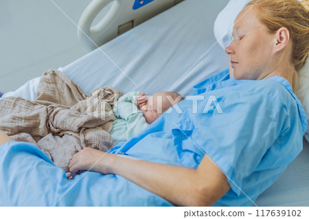 A baby lies with the mother after childbirth, resting peacefully. The serene moment captures the bond between mother and child as they begin their journey together. The hospital environment ensures a 117639102