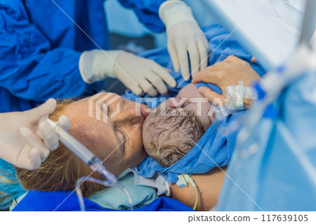 Baby on mother's chest immediately after birth in a hospital. The mother and newborn share a tender moment, emphasizing the bond and emotional connection. The medical staff ensures a safe and caring 117639105