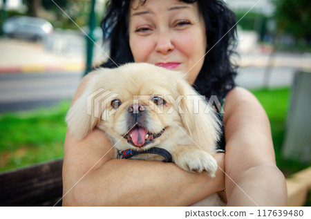 Golden Years Made Brighter: Woman's Outdoor Moment with Pekingese Demonstrates the Power of Animal Companionship. 117639480