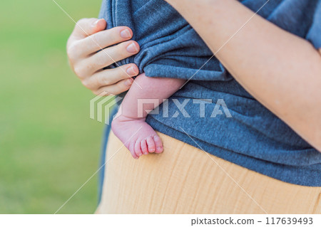 Mom walks with her newborn baby in a sling. This moment highlights the close bond between mother and child, promoting comfort, security, and the benefits of babywearing in everyday life Mom walks with her newborn baby in a sling. This moment highlights the close bond between mother and child, promoting comfort, security, and the benefits of babywearing in everyday life 117639493