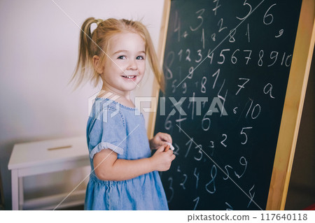 Young girl happily writing numbers on chalkboard in classroom setting  117640118