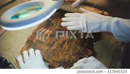 Close up of two archaeologists opening ancient Egyptian papyrus Close up of two archaeologists opening ancient Egyptian papyrus 117640329
