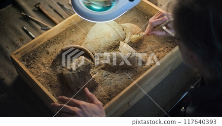 Close up of archaeologist cleaning cultural heritage under lamp, using brush 117640393