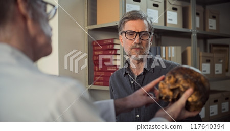 Two archaeologists analyze skull of ancient extinct human, have discussion 117640394