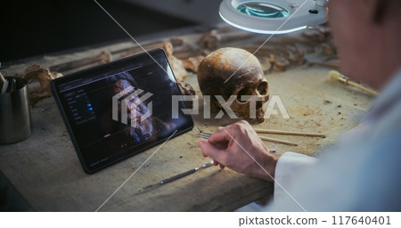 Two scientists examine fossil skull, discuss 3D model displayed on tablet screen Two scientists examine fossil skull, discuss 3D model displayed on tablet screen 117640401