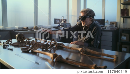 Archaeologist in VR headset conducts scientific research, studies remains of skeleton Archaeologist in VR headset conducts scientific research, studies remains of skeleton 117640549