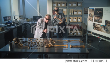 Two archaeologists in VR headsets study remains of ancient extinct human skeleton 117640591