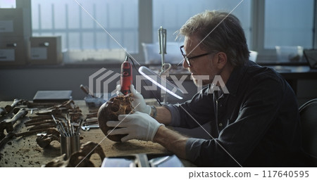 Mature archaeologist cleans fossil remains using professional tools 117640595