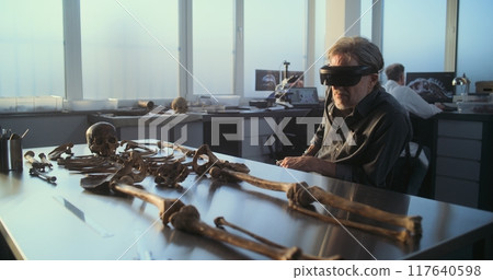 Archaeologist in VR headset conducts scientific research, studies remains of skeleton 117640598