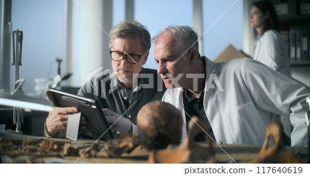 Mature archaeologist uses tablet computer and talks to colleague 117640619
